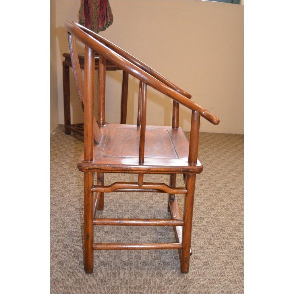 Side view of a wooden Horseshoe Chair with angled armrests on patterned carpet in a beige-walled room.