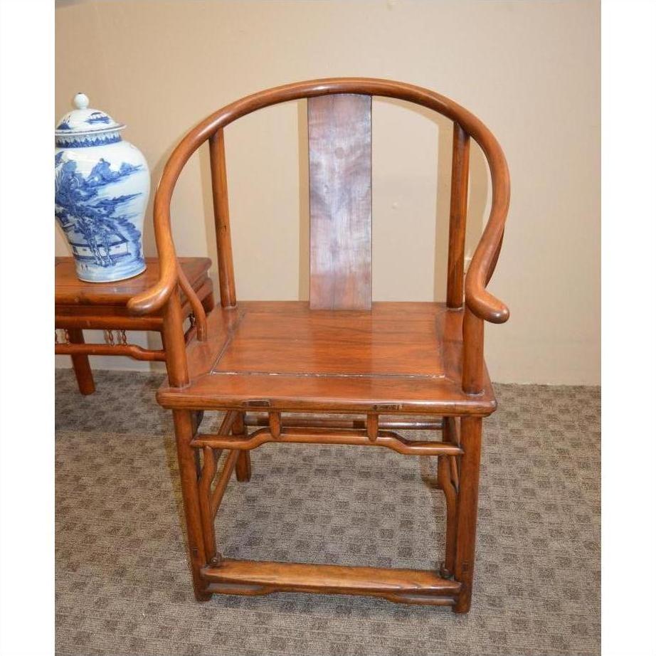 Brown wood Horseshoe Chair with rounded backrest beside a table holding a blue and white ceramic vase.