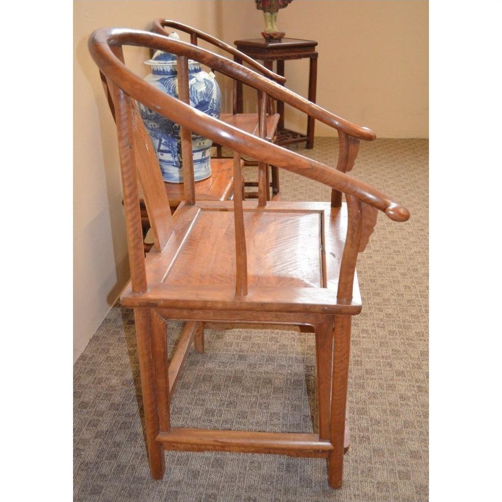 Wooden horseshoe chair with curved backrest and arms on carpet, near a blue and white ceramic vase.