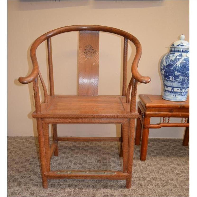 Dark wood horseshoe chair with curved backrest beside blue and white porcelain vase on wooden table.