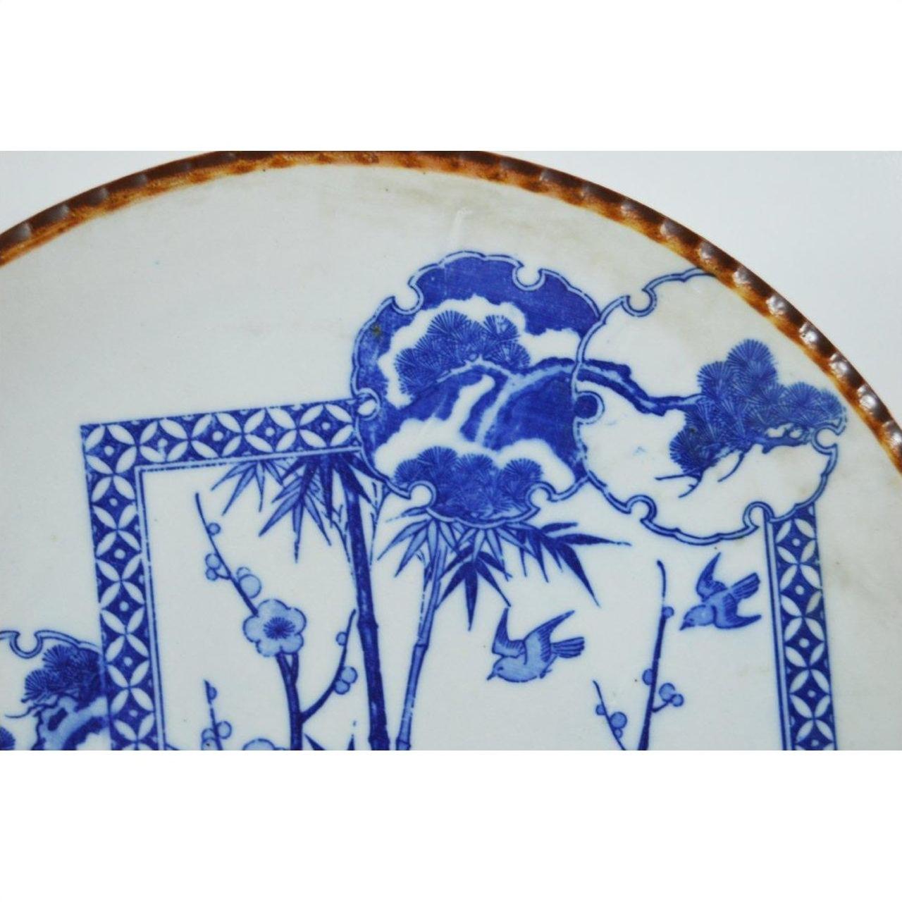 Close-up of blue and white porcelain Igezara transferware plate with floral, bird, landscape motifs and iron-brown ridged edge.