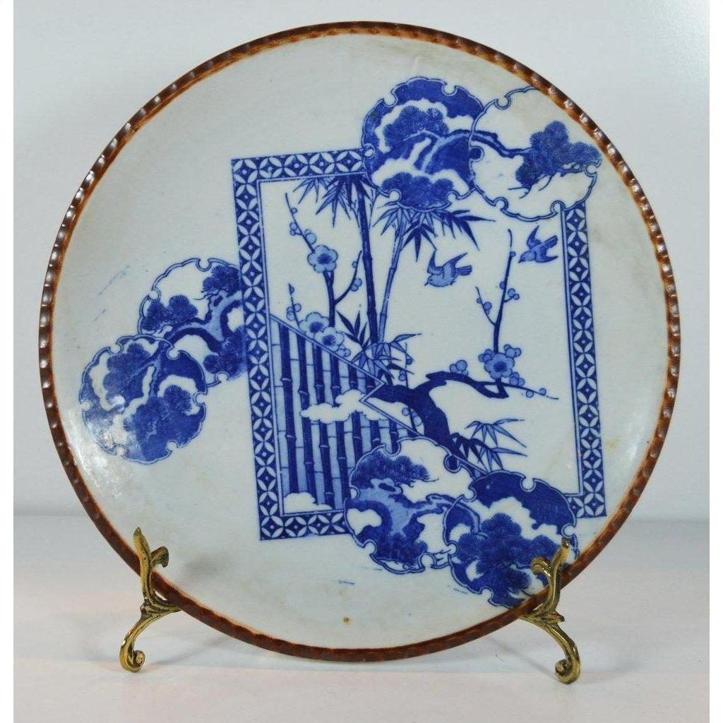 White ceramic Igezara transferware plate with blue floral and bamboo motifs on a brass stand.