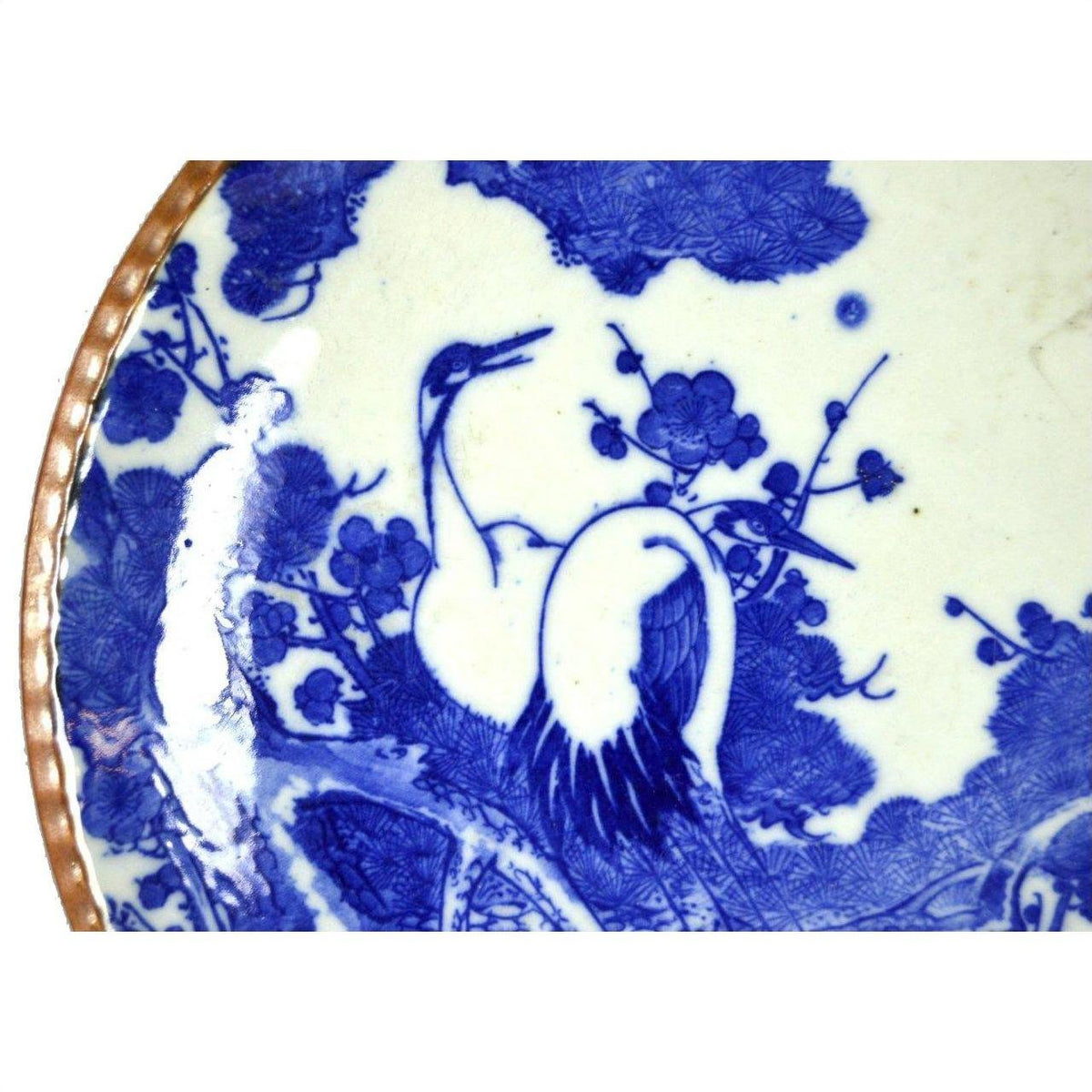 Blue and white ceramic Igezara transferware plate with crane and flower design, brown rim visible on left edge.