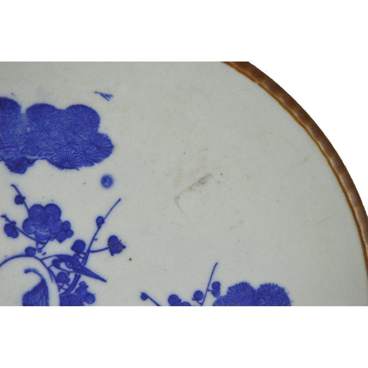 Close-up of blue and white ceramic Igezara Transferware plate with brown rim on a white background.