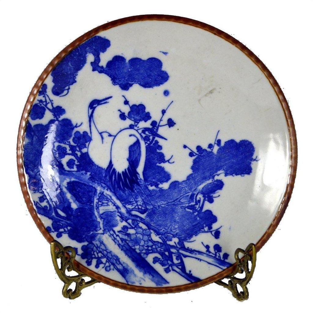 Blue and white ceramic Igezara transferware plate with crane and tree design on a metal stand.