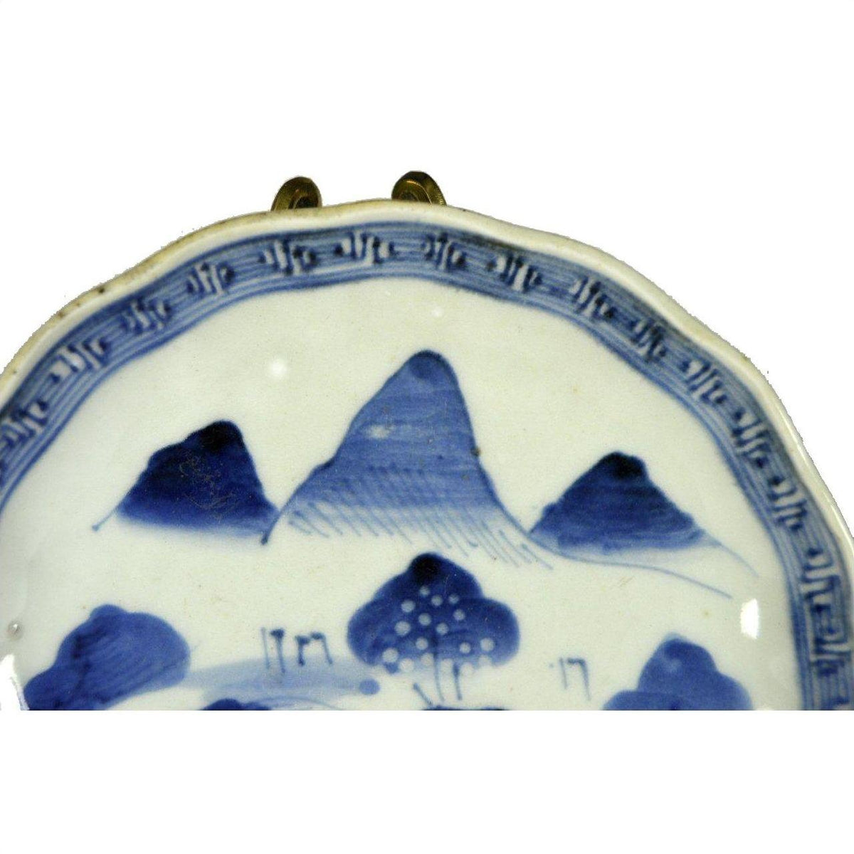 Blue and white ceramic Imari plate with hand-painted mountains, trees, and a patterned rim, close-up view.