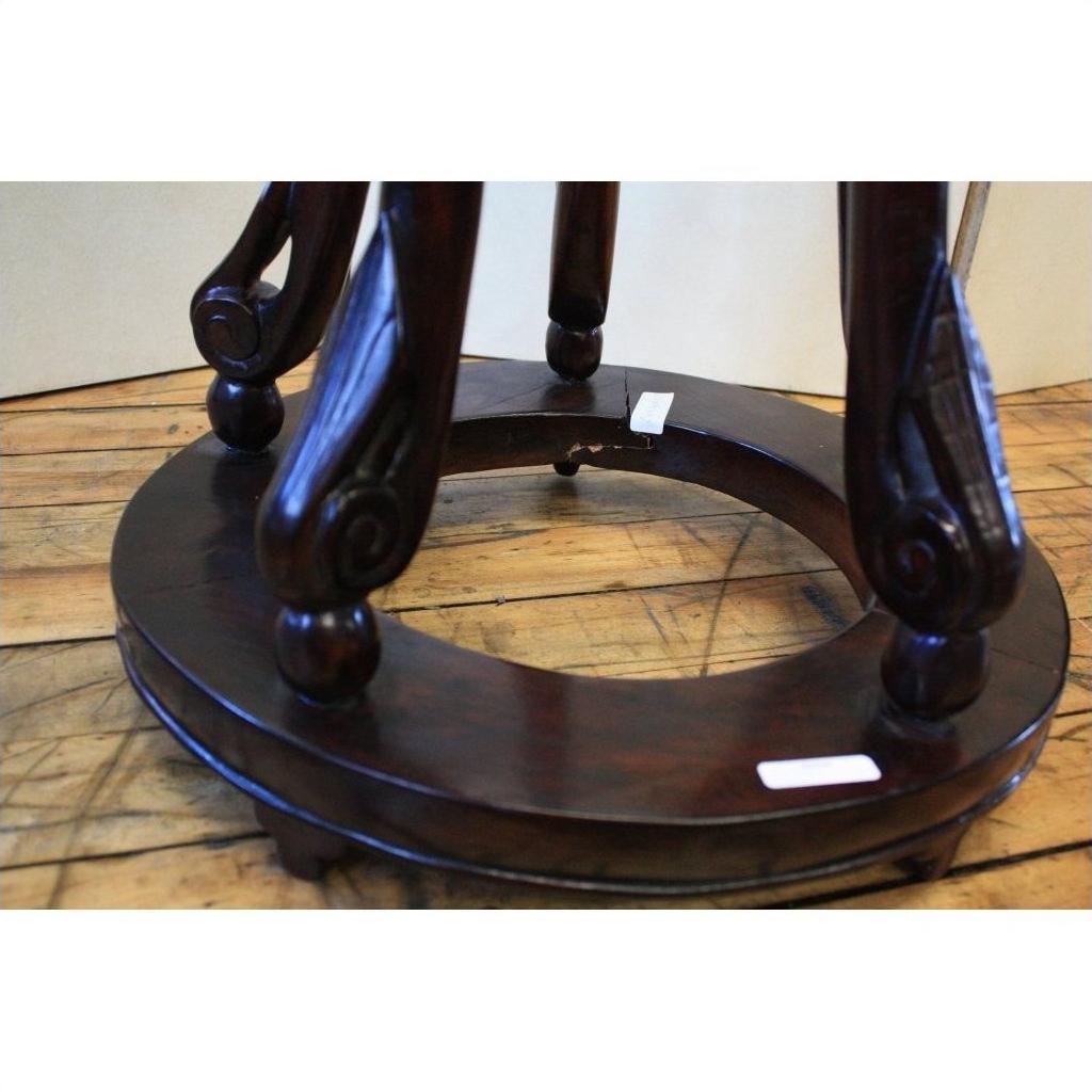 Close-up of antique dark brown lacquer incense stand with ornate curved legs on circular wood support, on wooden floor.