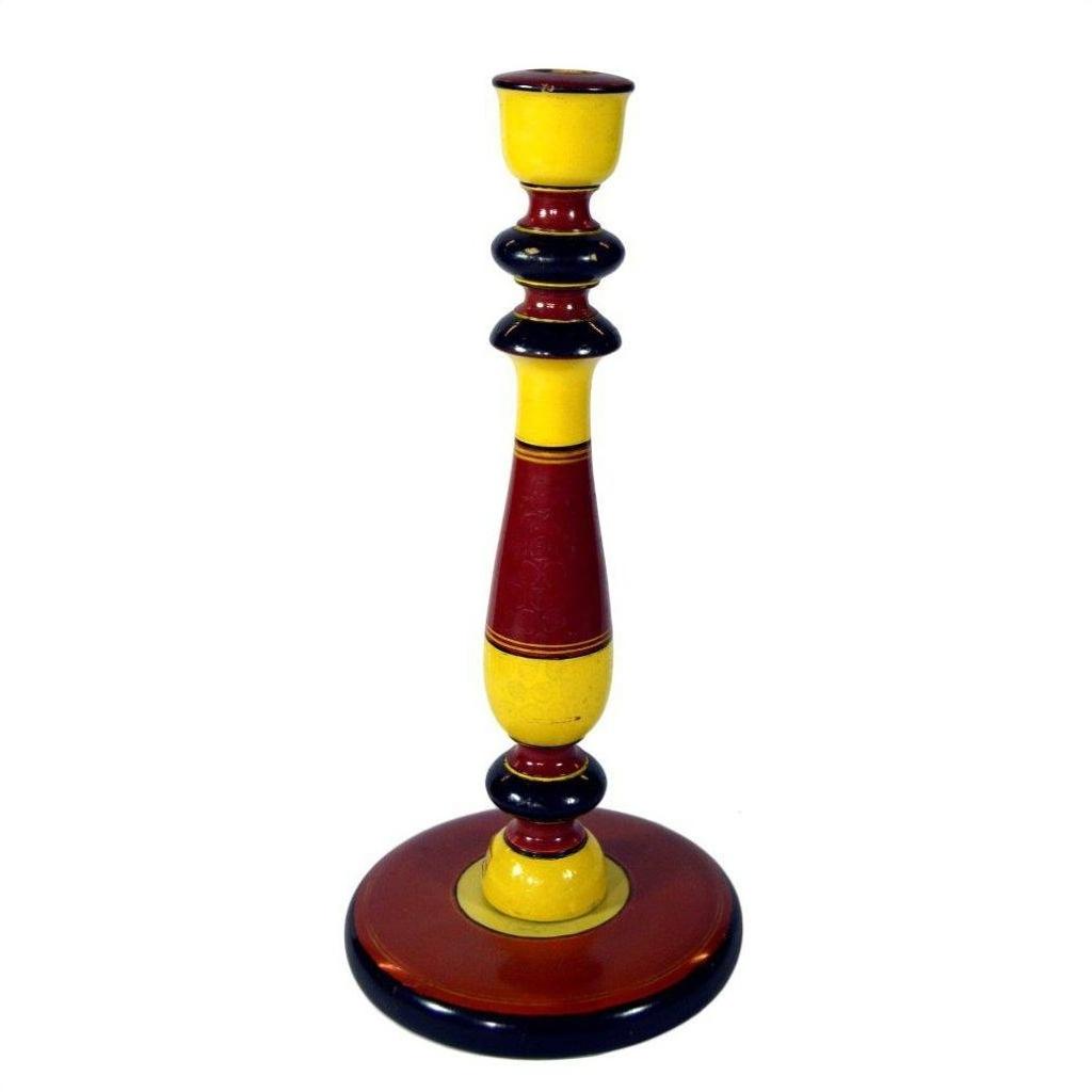 Close-up of tall, hand-carved wooden candlestick holder painted yellow, red, and black with a broad round base.