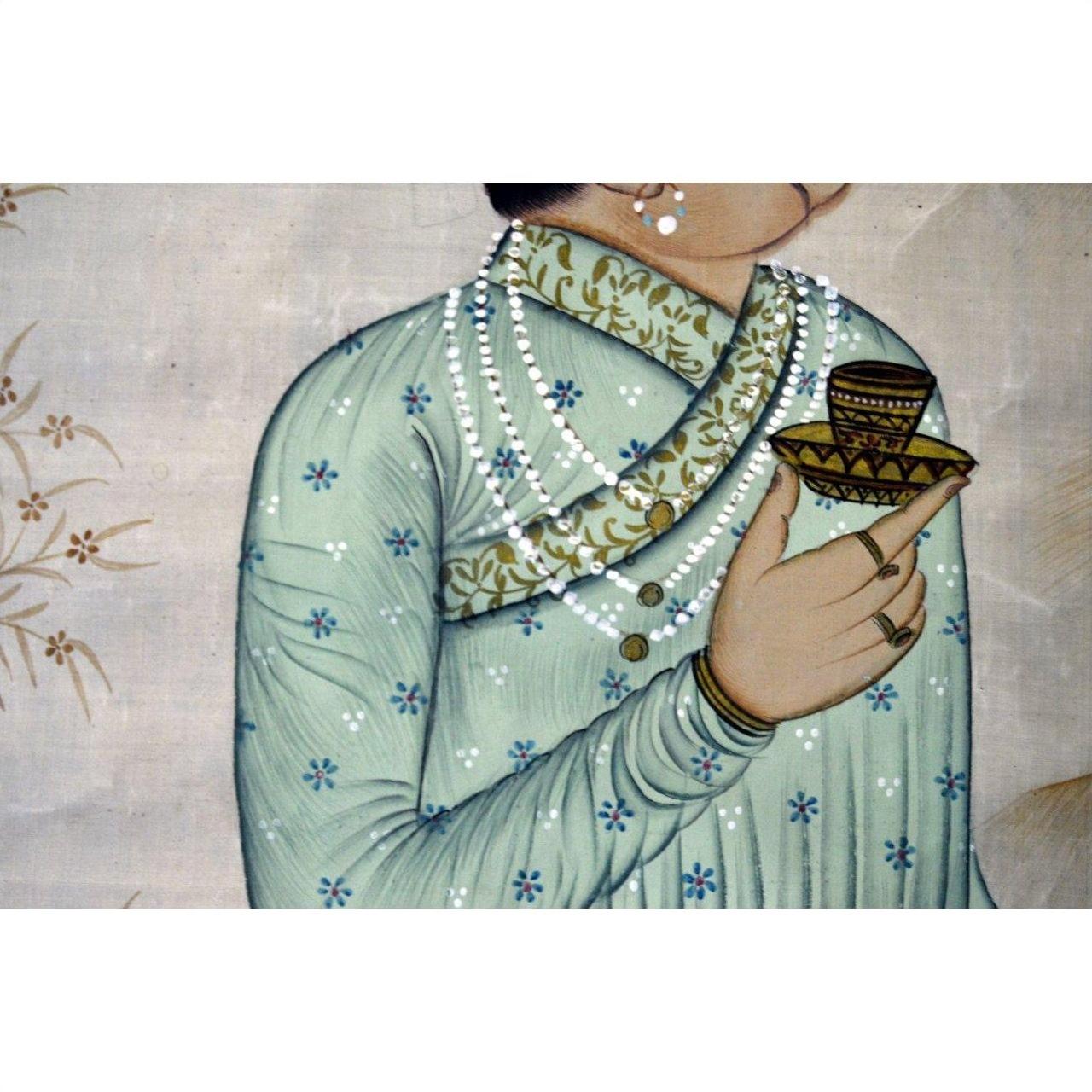 Close-up of a person’s torso and hand wearing multicolored silk tapestry, holding a decorated cup and saucer.