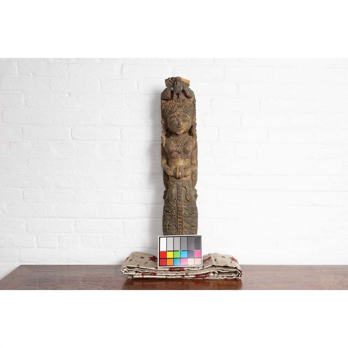 Colorful polychrome hand-carved wood statue of Indian celestial musician, shown with color chart by white brick wall.