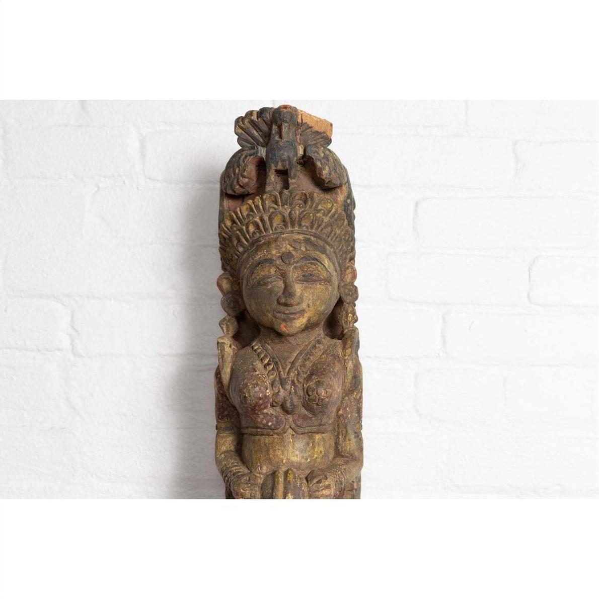 Polychrome wooden hand carved Indian antique statue of celestial musician against a white brick wall background.