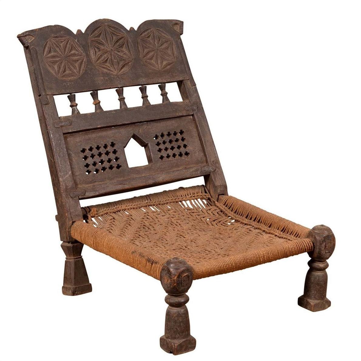 Brown wooden low seat chair with carved rosette details and handwoven rope seat, rustic antique style.