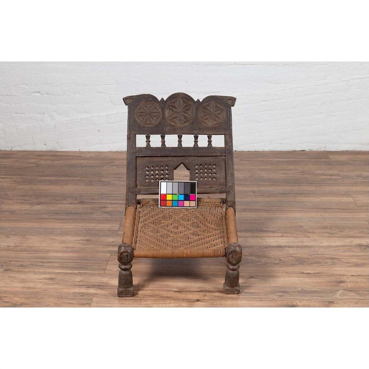 Brown wooden antique low seat chair with carved rosettes and rope seat, color calibration card on the seat.