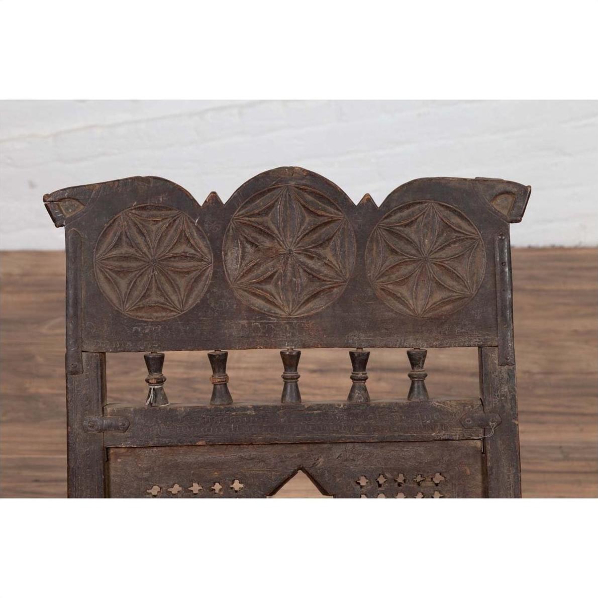 Close-up of a brown wooden Indian antique low seat chair with carved rosettes and woven rope seat.