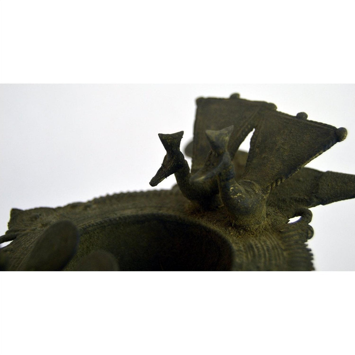 Close-up of a brass oil burner with two stylized birds on the rim of a 13-inch vase, indoors.