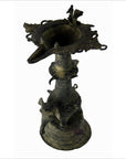 Close-up of dark brass Indian oil burner with intricate carvings and animal-shaped figures on the sides.