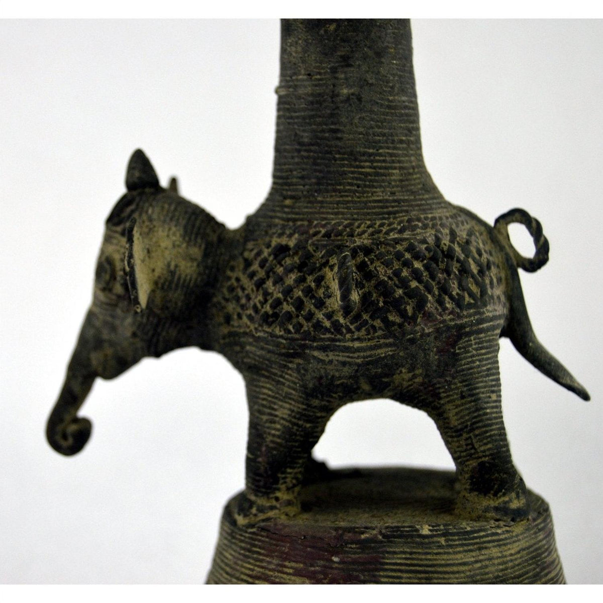 Close-up of a small, textured brass Indian oil burner next to a patterned collectible vase on a surface.