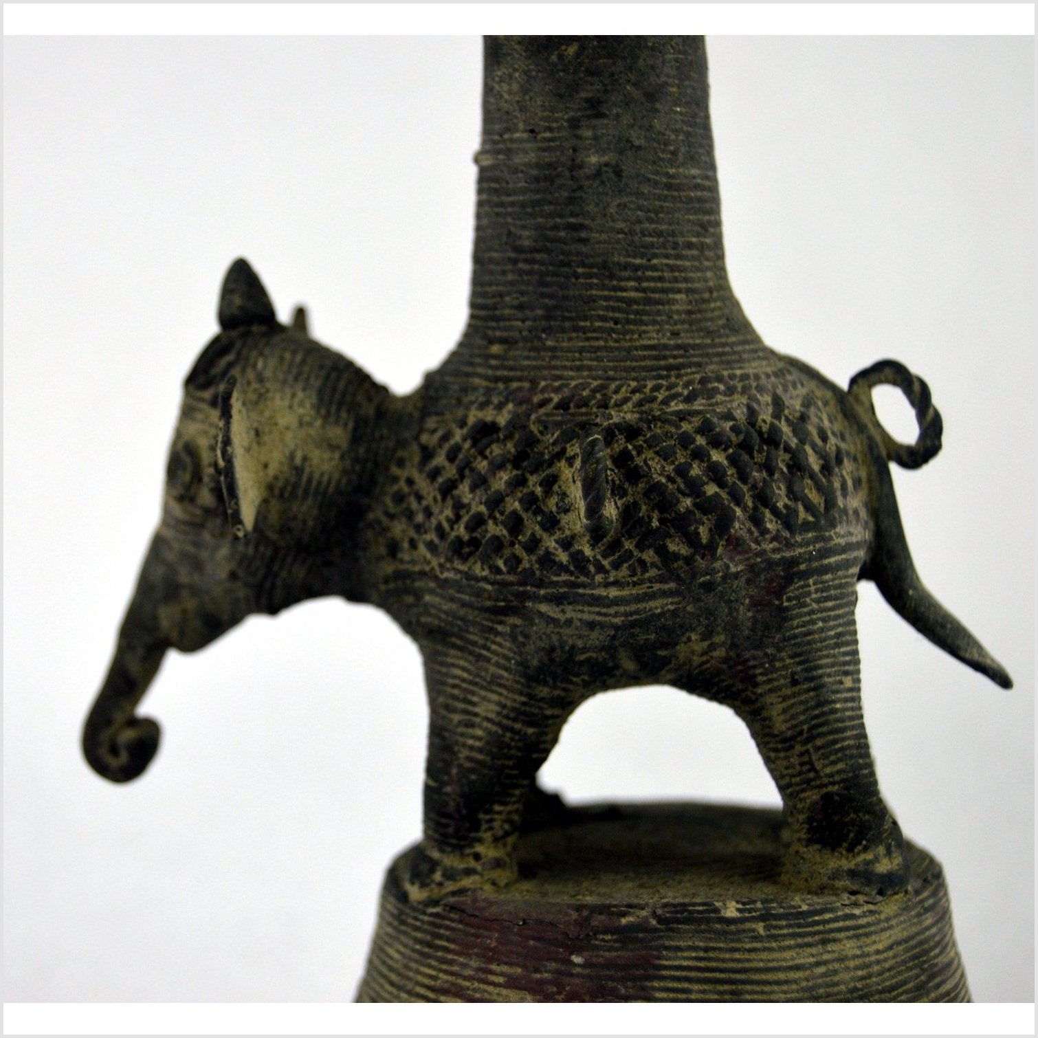 Close-up of a small, textured brass Indian oil burner next to a patterned collectible vase on a surface.