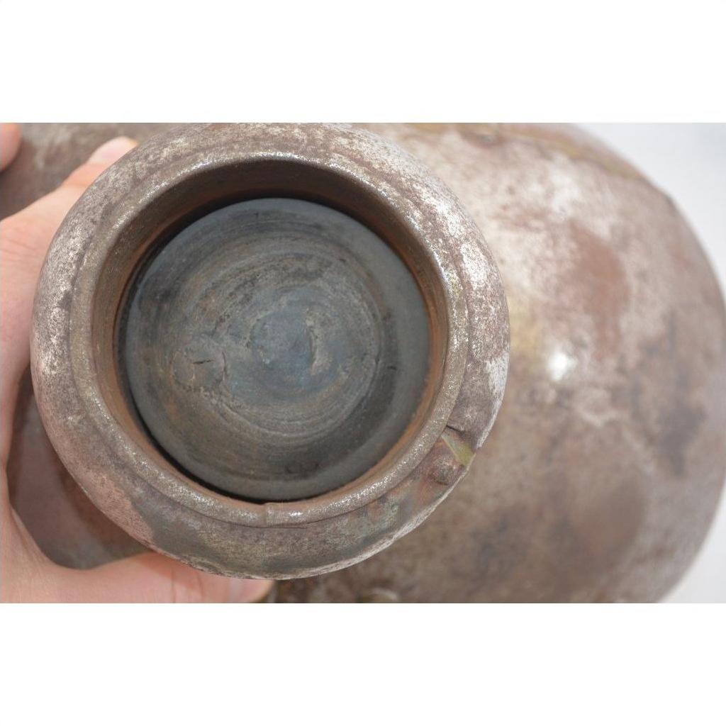 Close-up of a hand holding an oval silver metal Indian water jug, antique style.