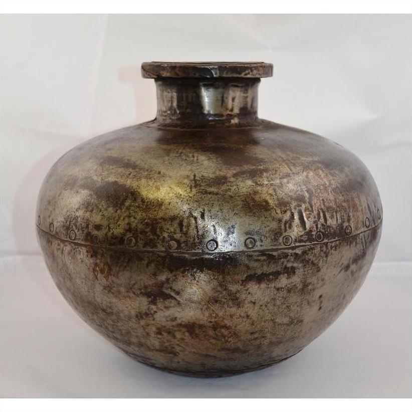 Close-up of a rustic metallic Indian water jug, round-shaped with a small neck and rivet-like details.