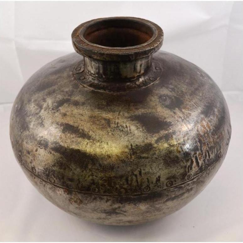 Close-up of a round, tarnished metal Indian water jug with wide neck on a plain background.