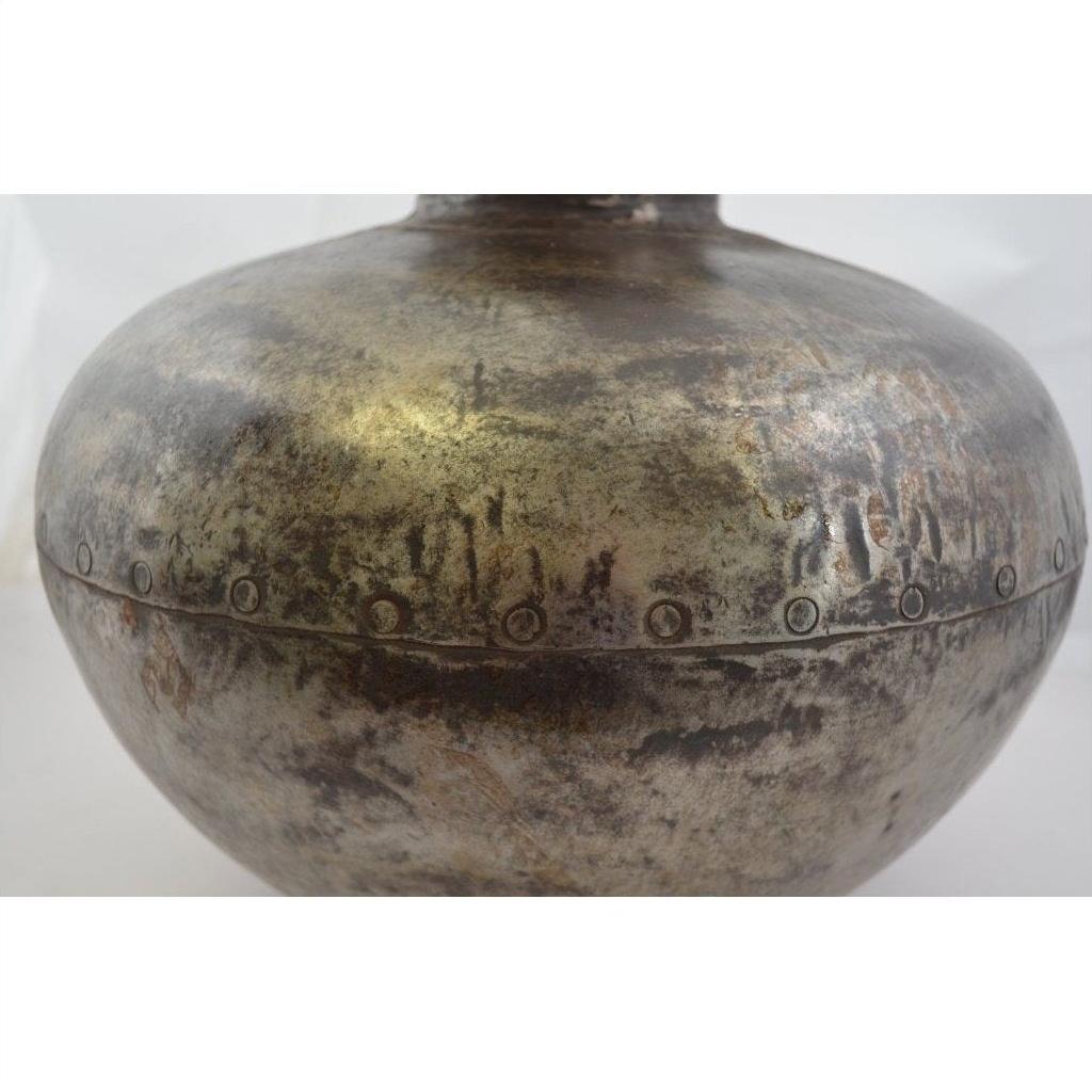Close-up of a silver metal Indian water jug with round shape, riveted seam, and tarnished textured surface.