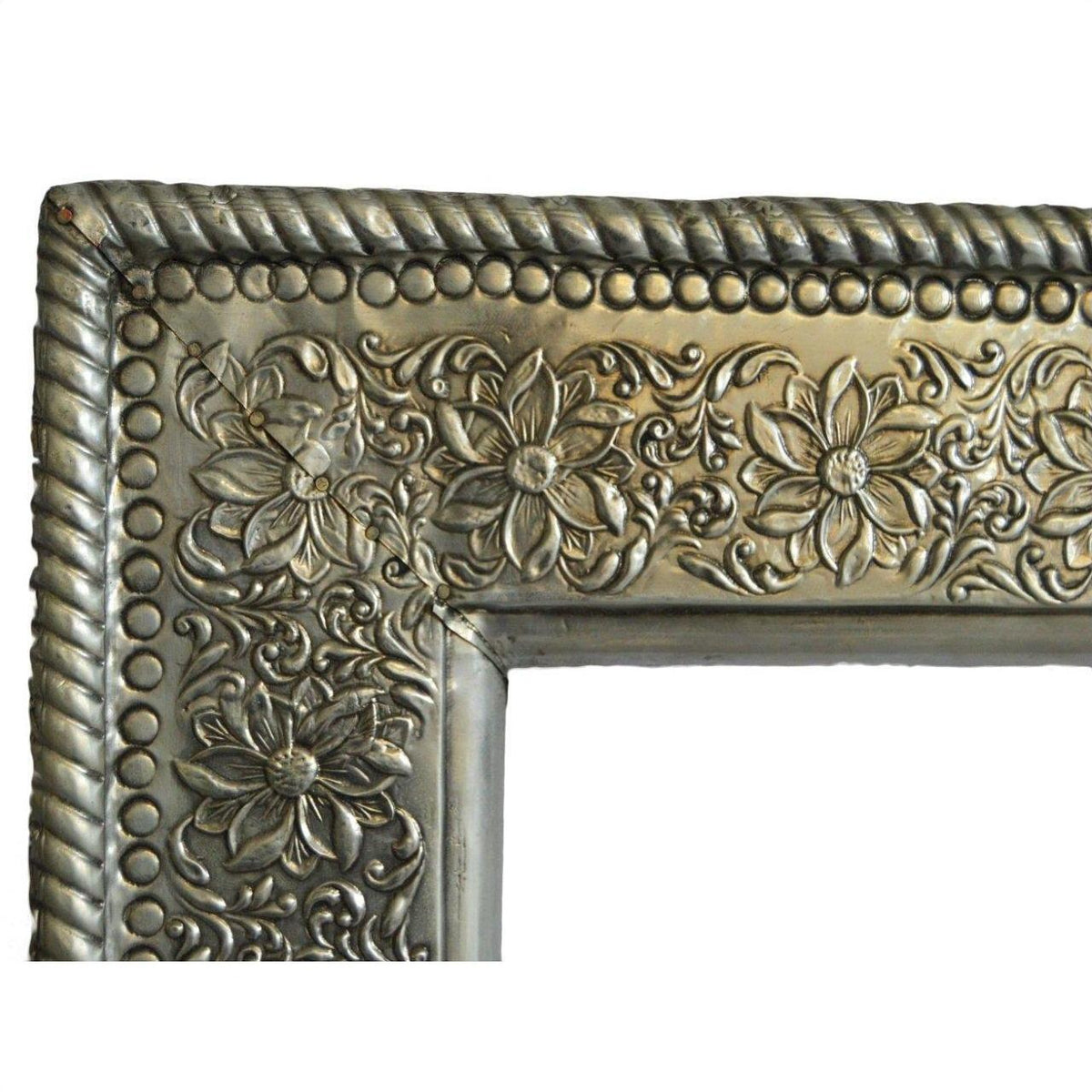 Close-up of silver-nickel Indian repoussé rectangular frame corner with embossed floral swirl detailing.
