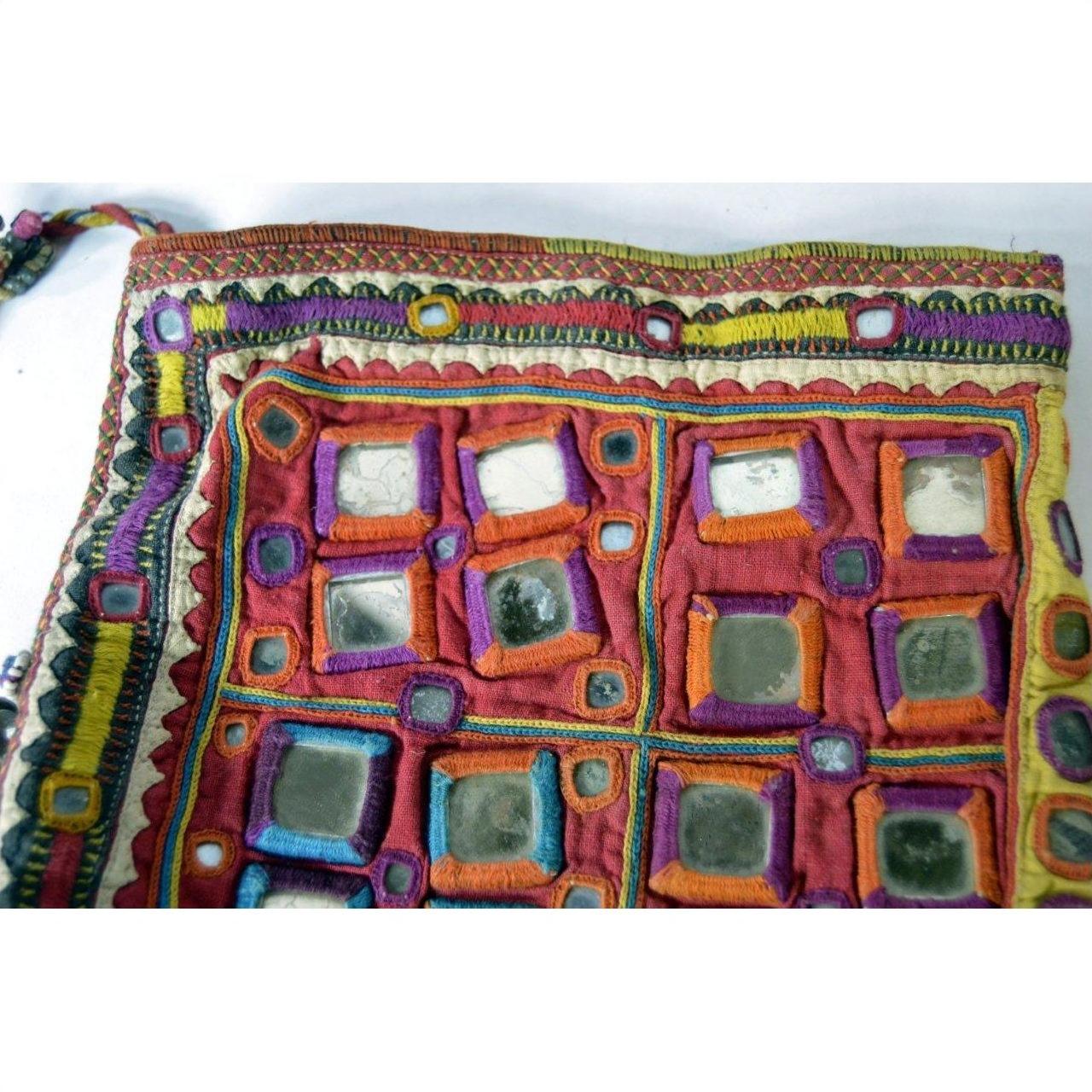 Close-up of a colorful embroidered Indian pouch with mirror accents and bright geometric patterns on fabric.