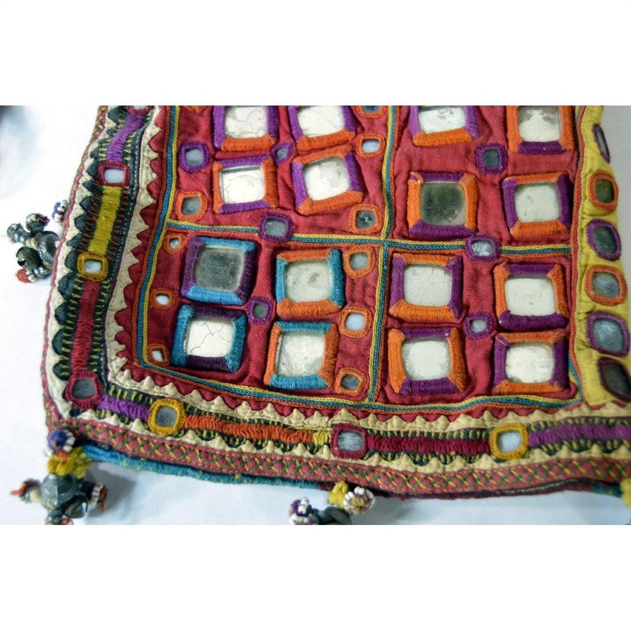Close-up of a multicolor embroidered fabric pouch with mirror accents and tassels, Indian traditional design.