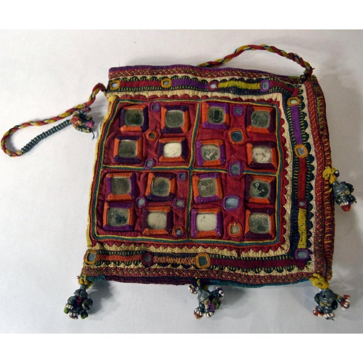 Red embroidered fabric pouch with mirror accents, tassels, and braided drawstrings on a white background, close-up.