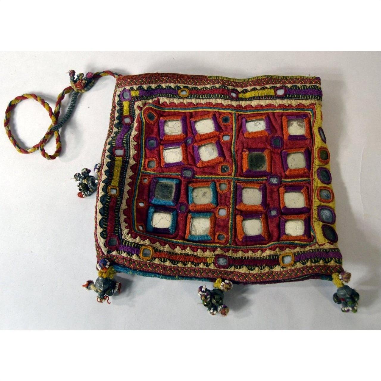 Colorful fabric square pouch with embroidery, mirror accents, braided strap, and tassels, close-up view.