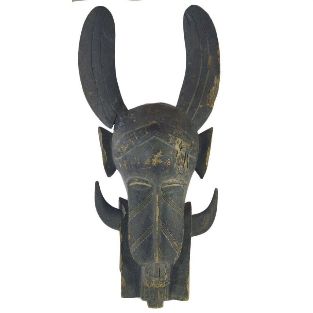 Brown wooden Indonesian hand carved figural shield with geometric carvings and tall curved horns, some visible cracks.