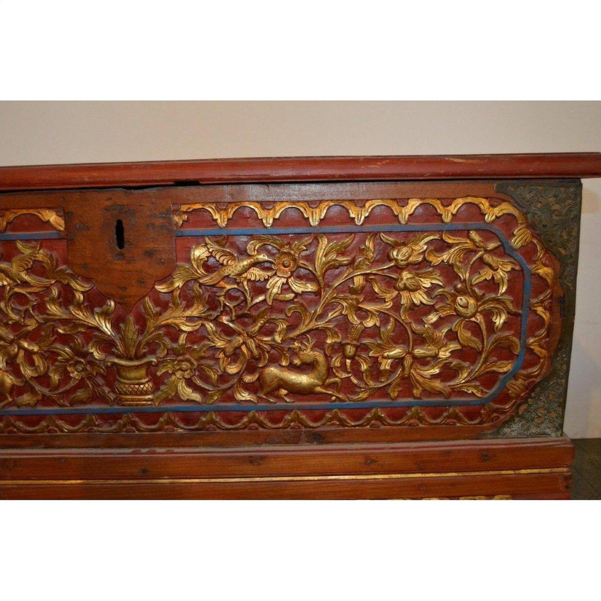 Red wood Indonesian Madura blanket chest with gold floral carving and vase, ornate detail, close-up.