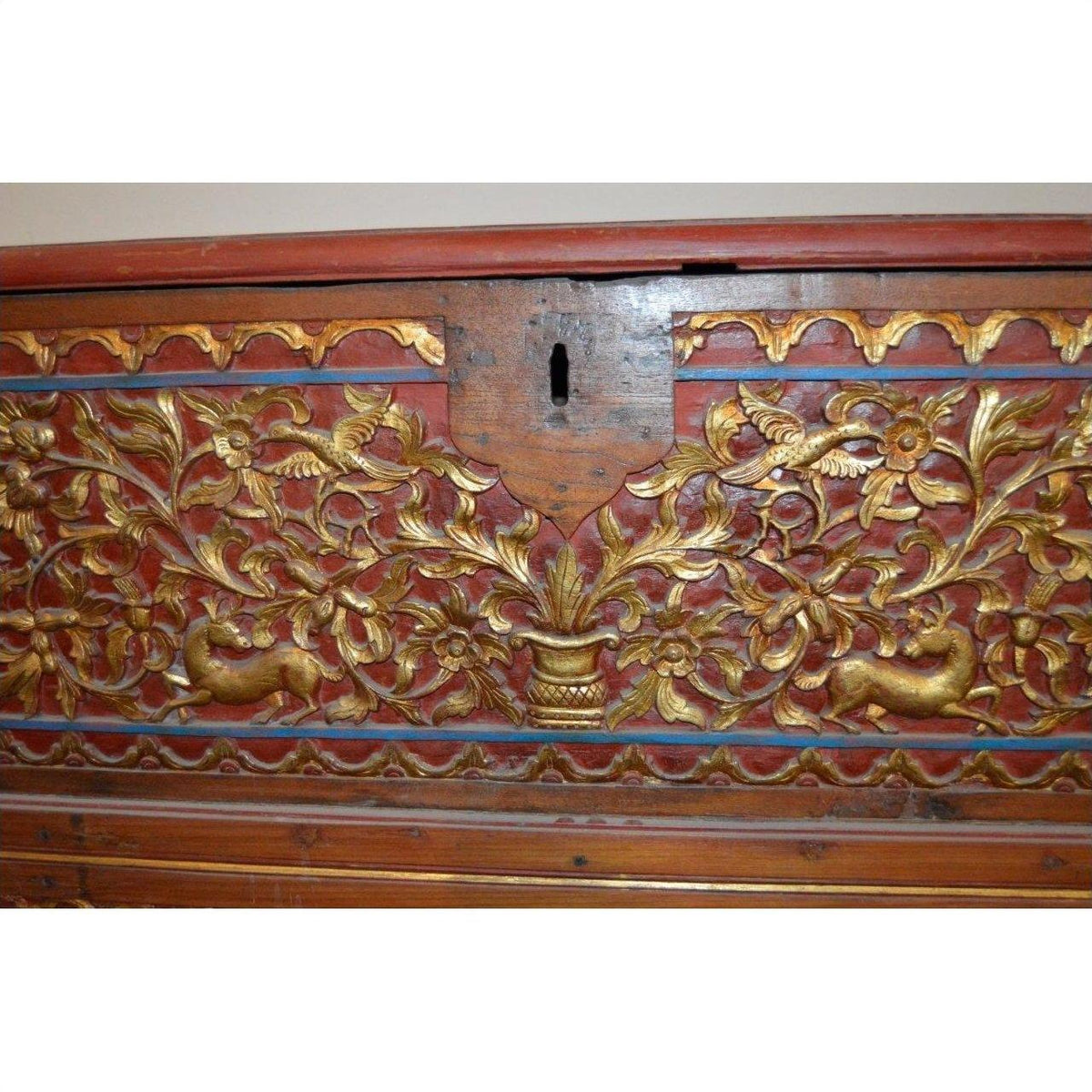 Brown wood Madura blanket chest with ornate gold floral and animal carvings, top keyhole, close-up view.