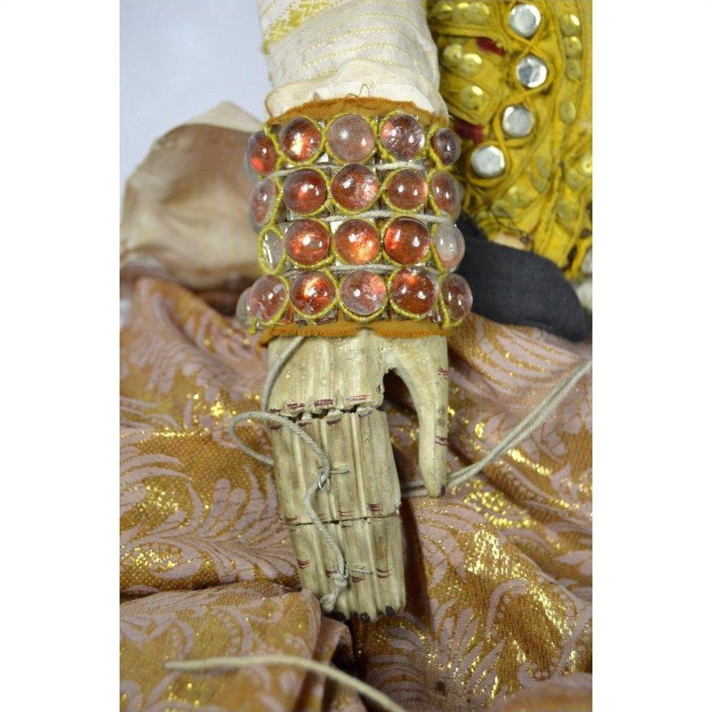 Close-up of gold jeweled cuff and articulated fingers on Indonesian puppet wearing patterned golden fabric clothing.