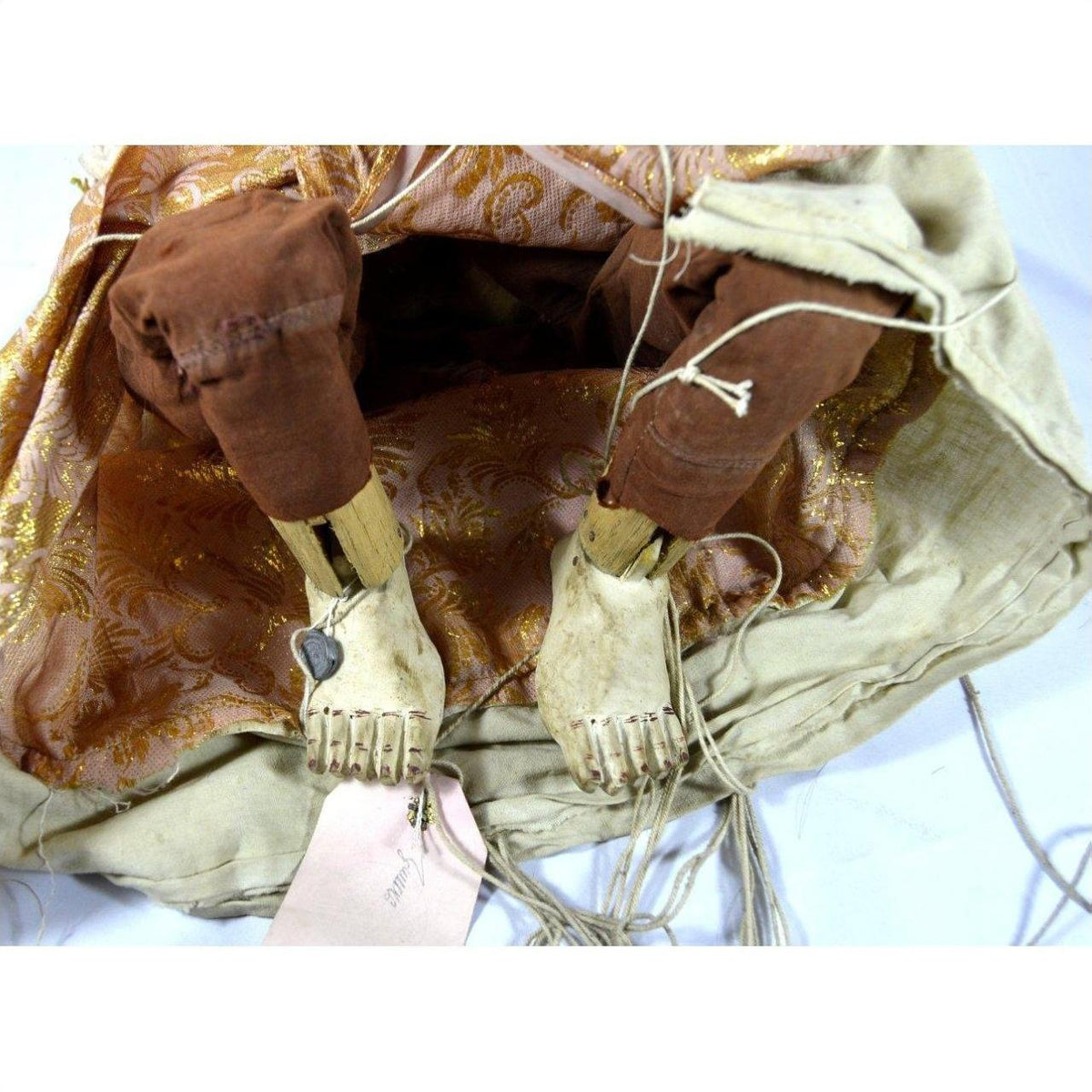 Close-up of wooden Indonesian puppet legs and feet with tangled strings, brown pants, and gold-patterned dress.