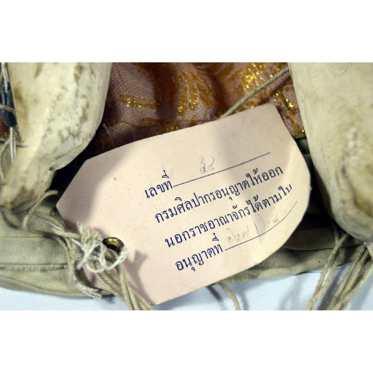 Close-up of handwritten Thai label with museum export permit on Indonesian puppet, paper attached to wood.