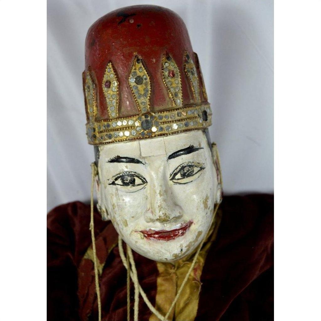Close-up of Indonesian puppet with tangled strings, red and gold hat, and red lips on a white background.