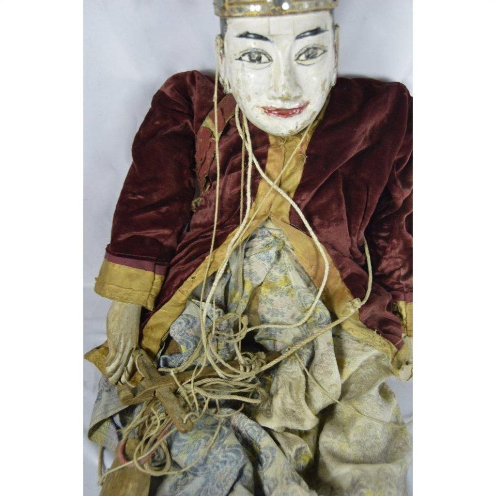 Close-up of Indonesian puppet with painted face, velvet jacket, patterned skirt, and tangled strings.