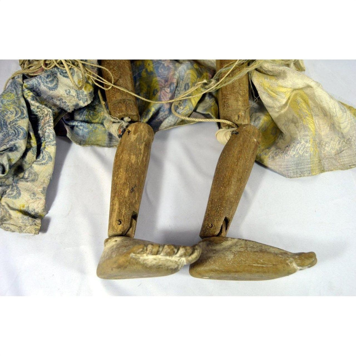 Brown wooden Indonesian puppet with jointed legs, patterned fabric clothing, lying on a white surface.