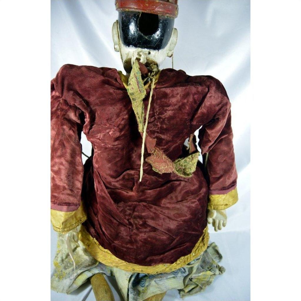 Red velvet Indonesian puppet with yellow trim and matching hat, viewed from the back.