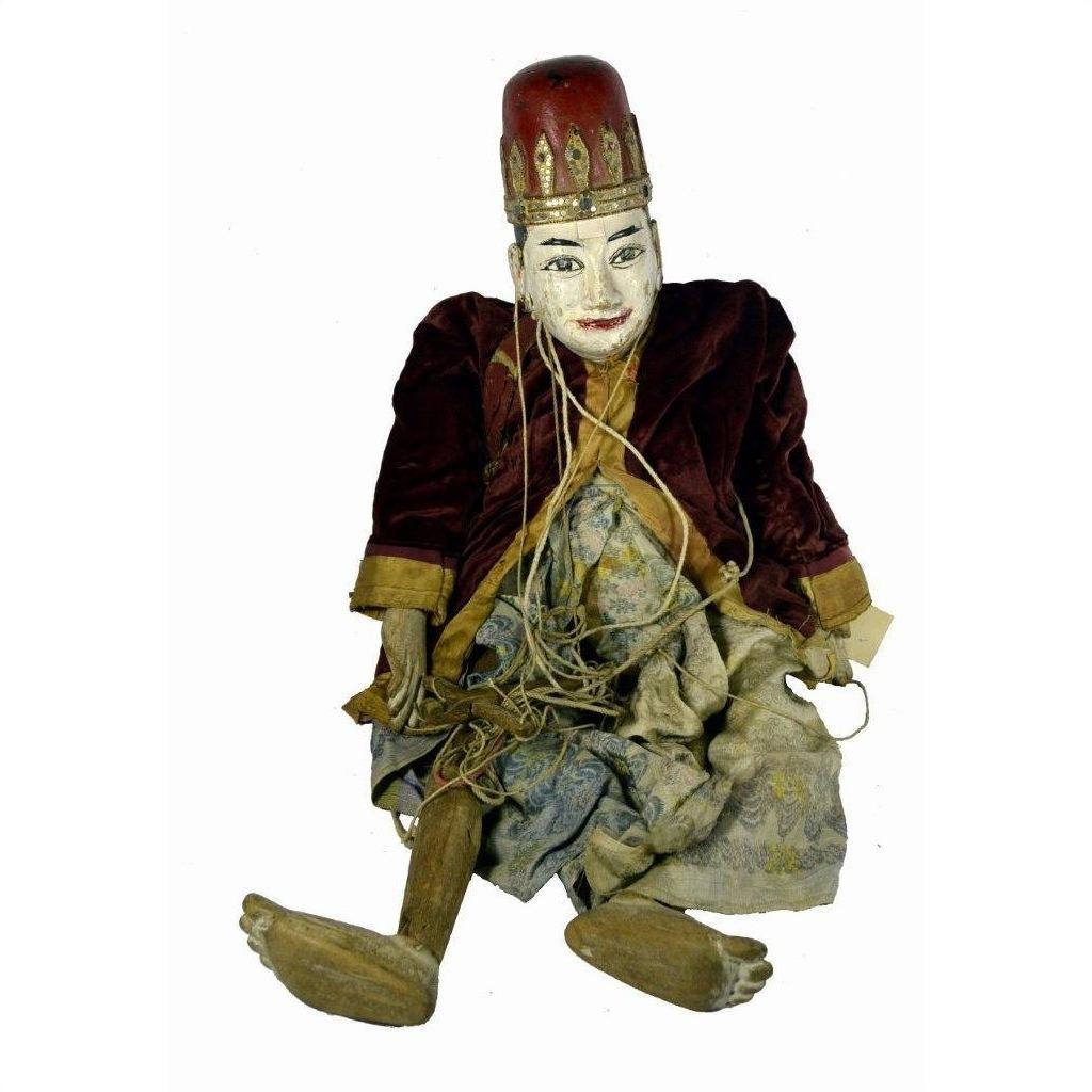 Close-up of painted Indonesian puppet with red hat, velvet jacket, and tangled limb strings, seated upright.