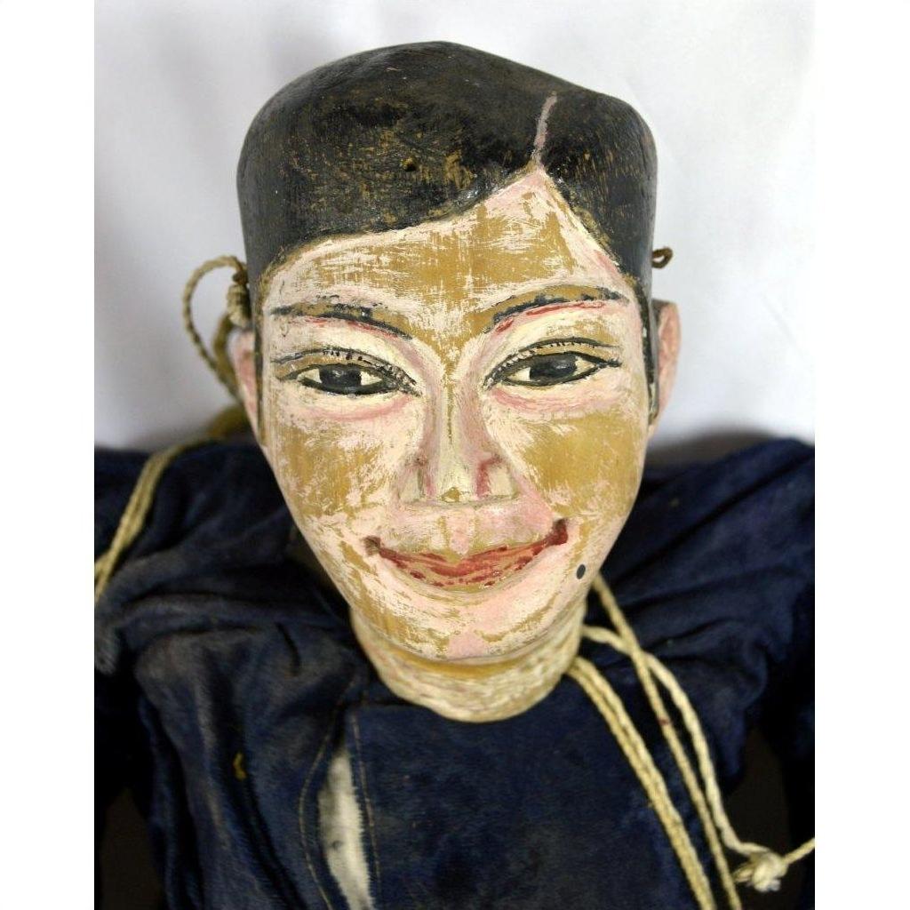 Close-up of Indonesian puppet with blue clothing, black hair, smiling face, and tangled strings on white background.