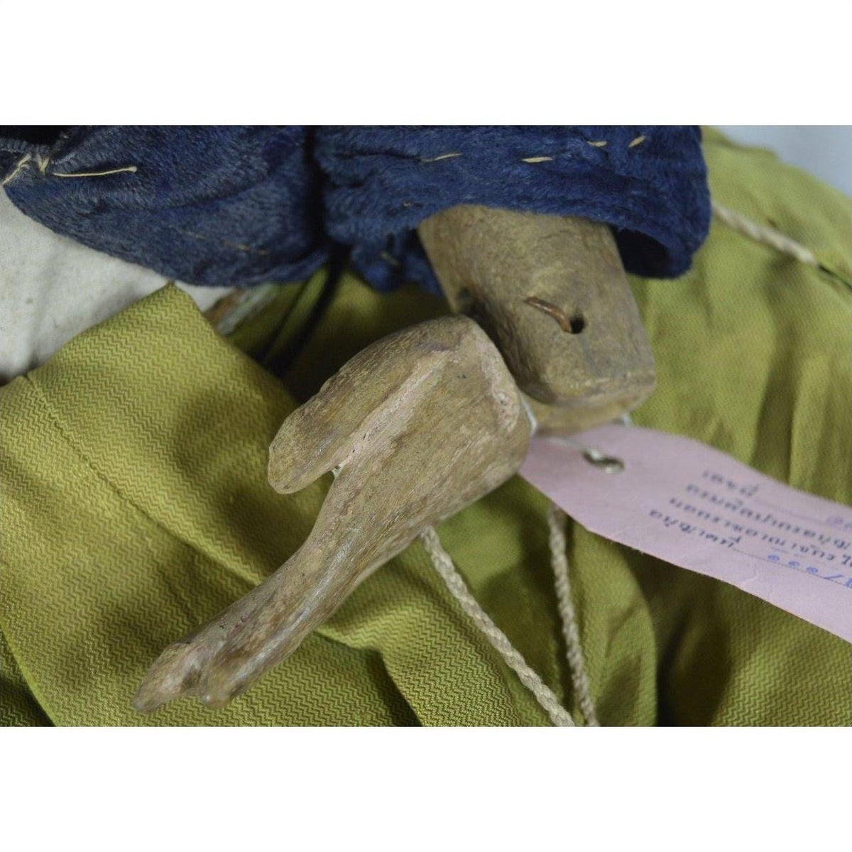 Close-up of wooden Indonesian puppet hand in yellow and blue fabric with tangled strings and pink wrist tag.