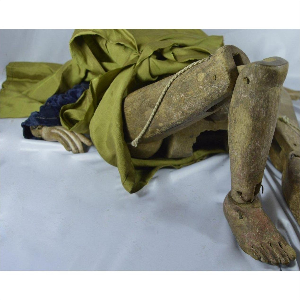 Close-up of Indonesian puppet with tangled strings, green cloth, worn legs and hand, lying on its side.
