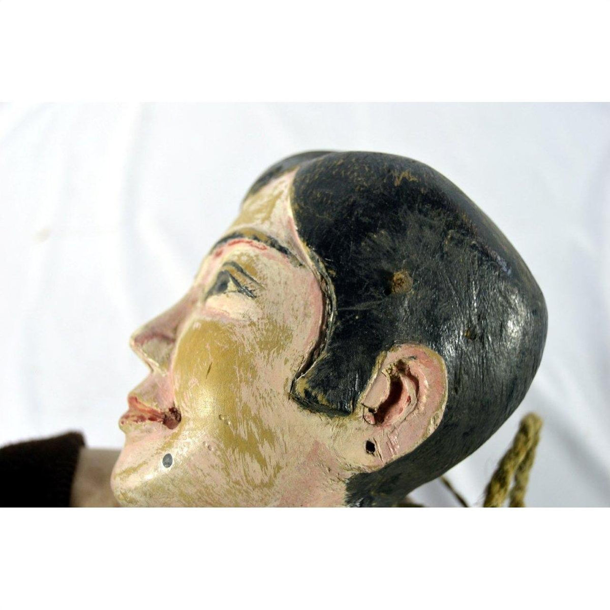 Close-up of Indonesian puppet head with black hair, tangled strings, and a smiling face on a white background.