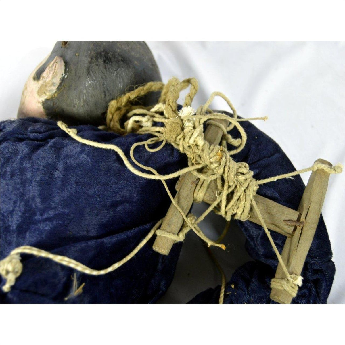 Close-up of blue fabric Indonesian puppet with tangled strings and one loose leg on white background.