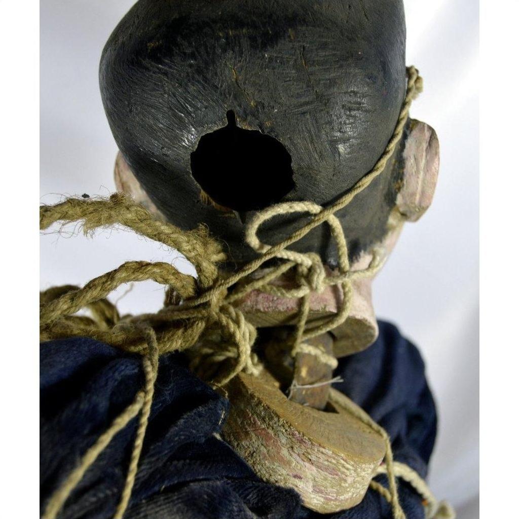 Brown wooden Indonesian puppet with tangled strings, one loose leg, ropes around neck and shoulders, rear view.