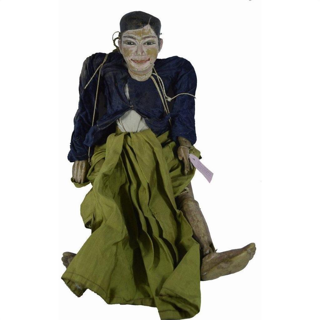 Close-up of Indonesian puppet with painted face, dark jacket, green skirt, tangled strings on white background.