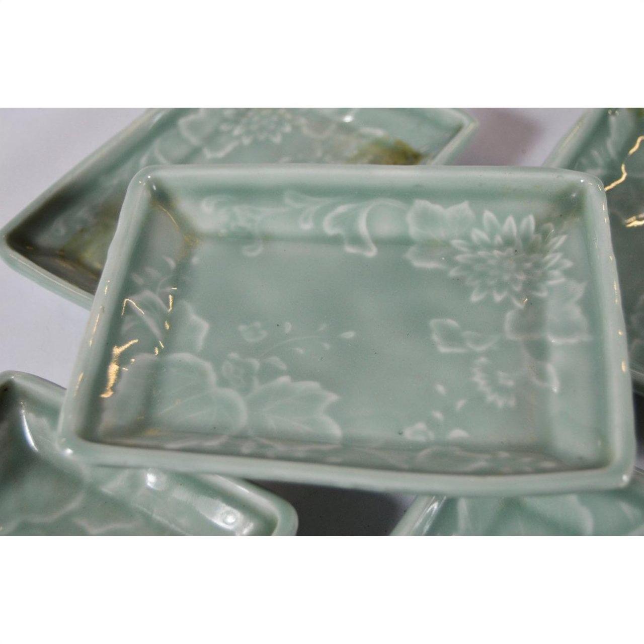 Light green celadon ceramic serving bowls with floral pattern, stacked and overlapping on a white surface.